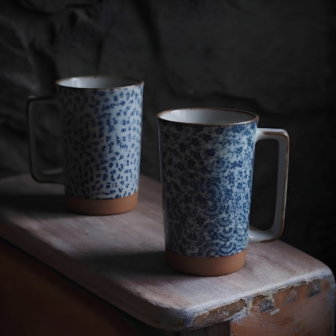 Deux mugs en céramique japonaise à motifs floraux bleus dans une ambiance chaleureuse.