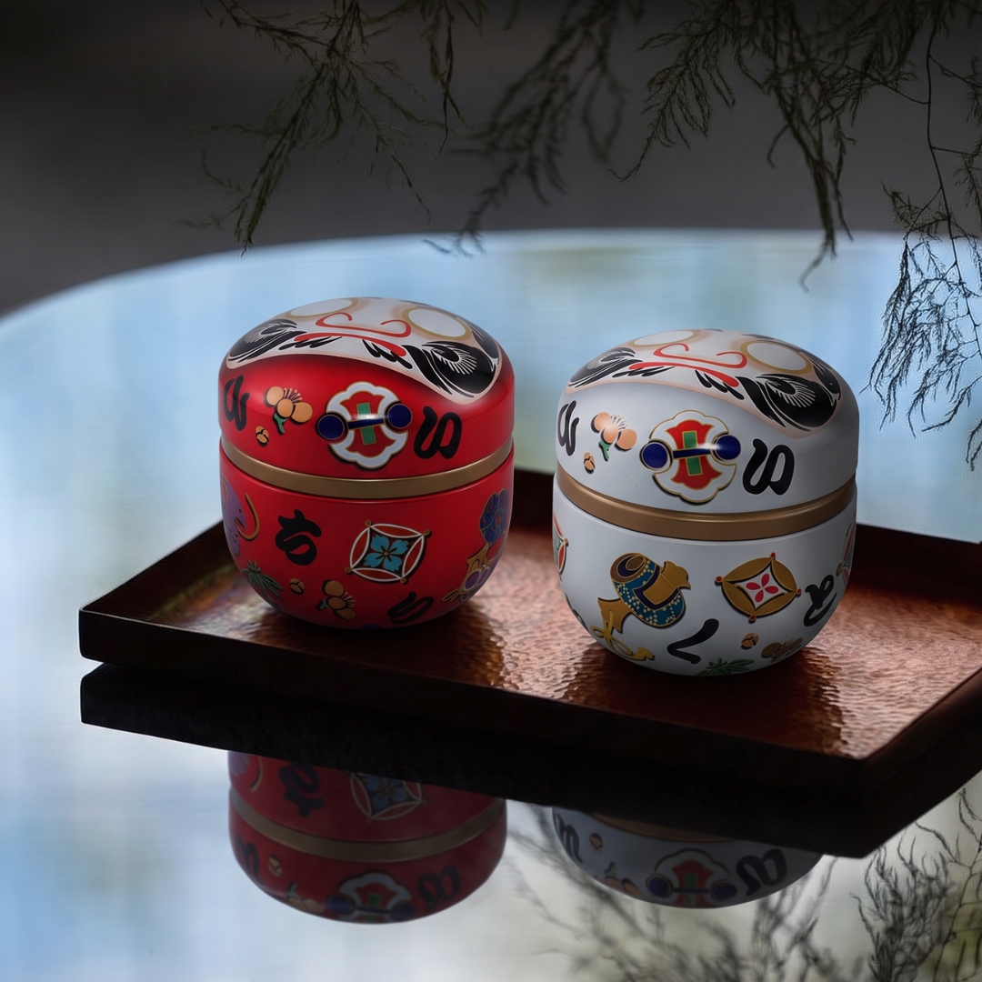 Boîtes à thé Yugen lab en fer blanc, modèles Daruma rouge et blanc avec motifs japonais sur un plateau en cuivre.
