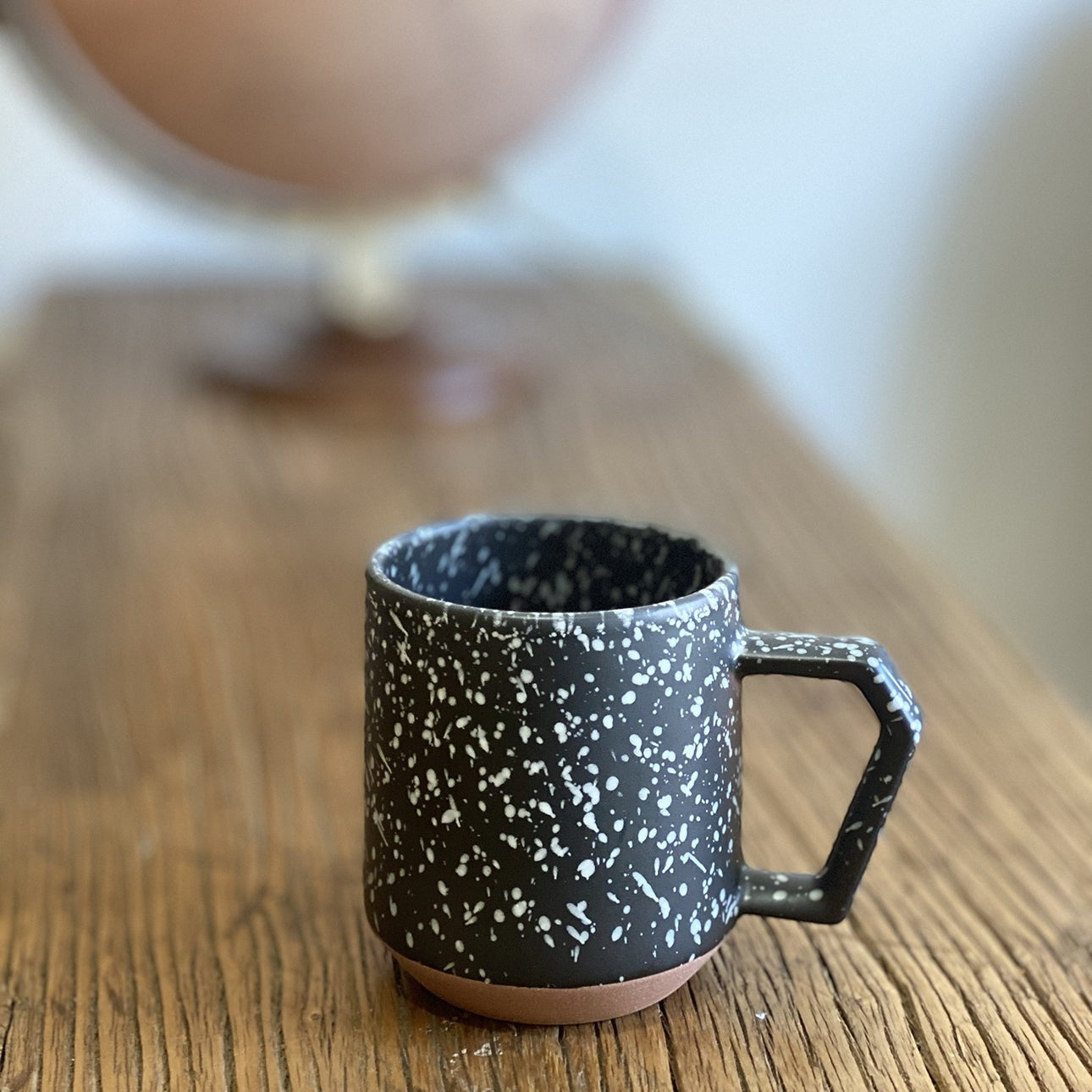 Mug Yugen lab en céramique noire avec motif moucheté blanc et anse géométrique sur une table en bois