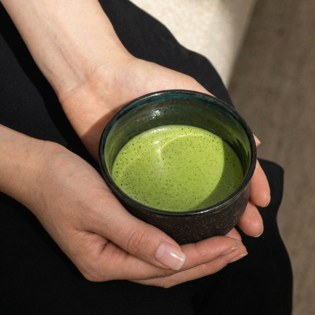 Bol matcha noir tenu dans les mains avec mousse de thé vert