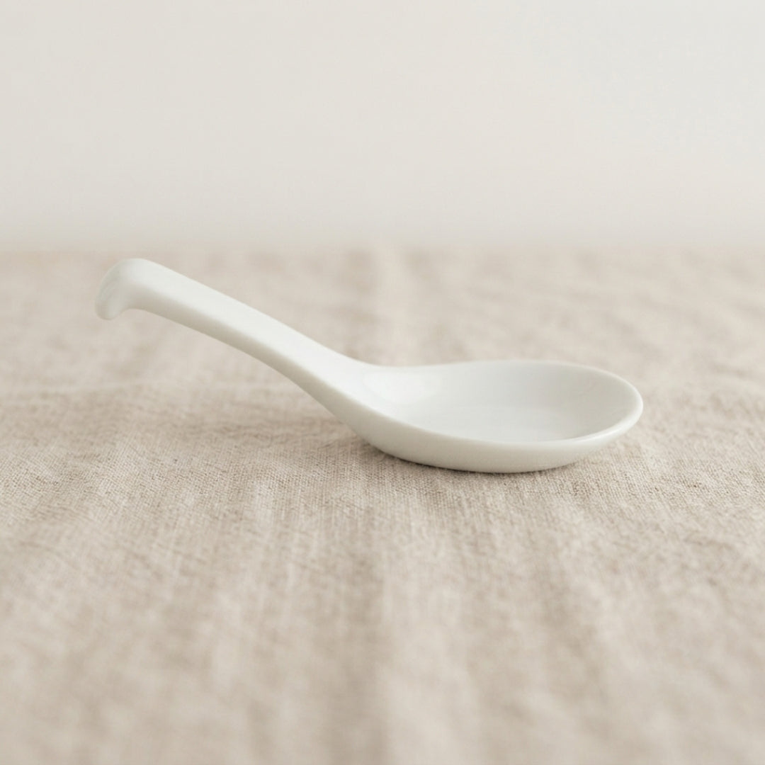 Cuillère blanche Classic en porcelaine posée sur un tissu naturel.