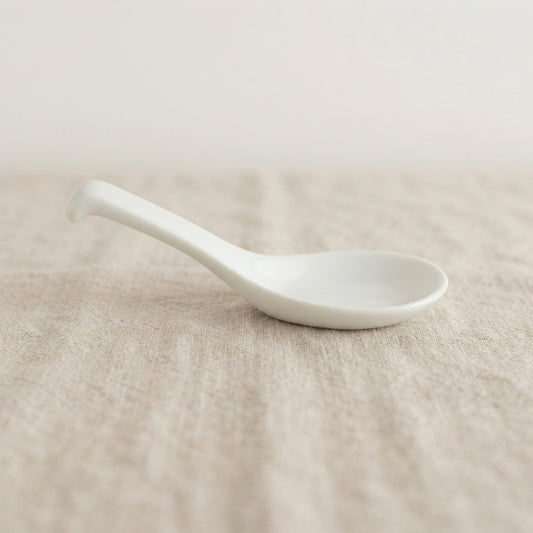 Cuillère blanche Classic en porcelaine posée sur un tissu naturel.