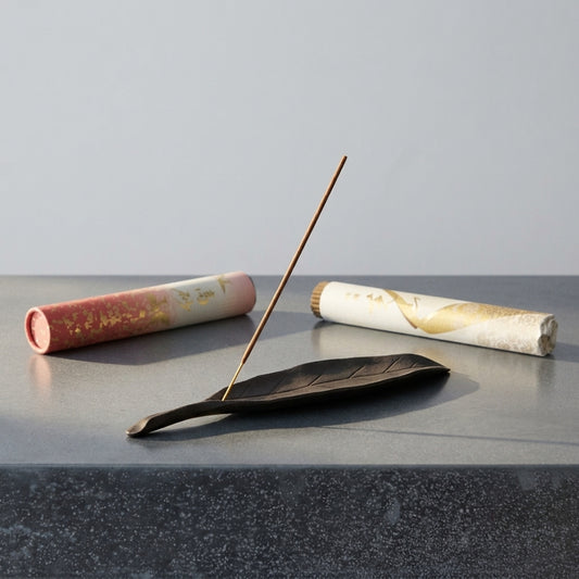 Porte-encens en forme de feuille avec bâtonnet d'encens allumé et rouleaux d'encens Kyara en arrière-plan.