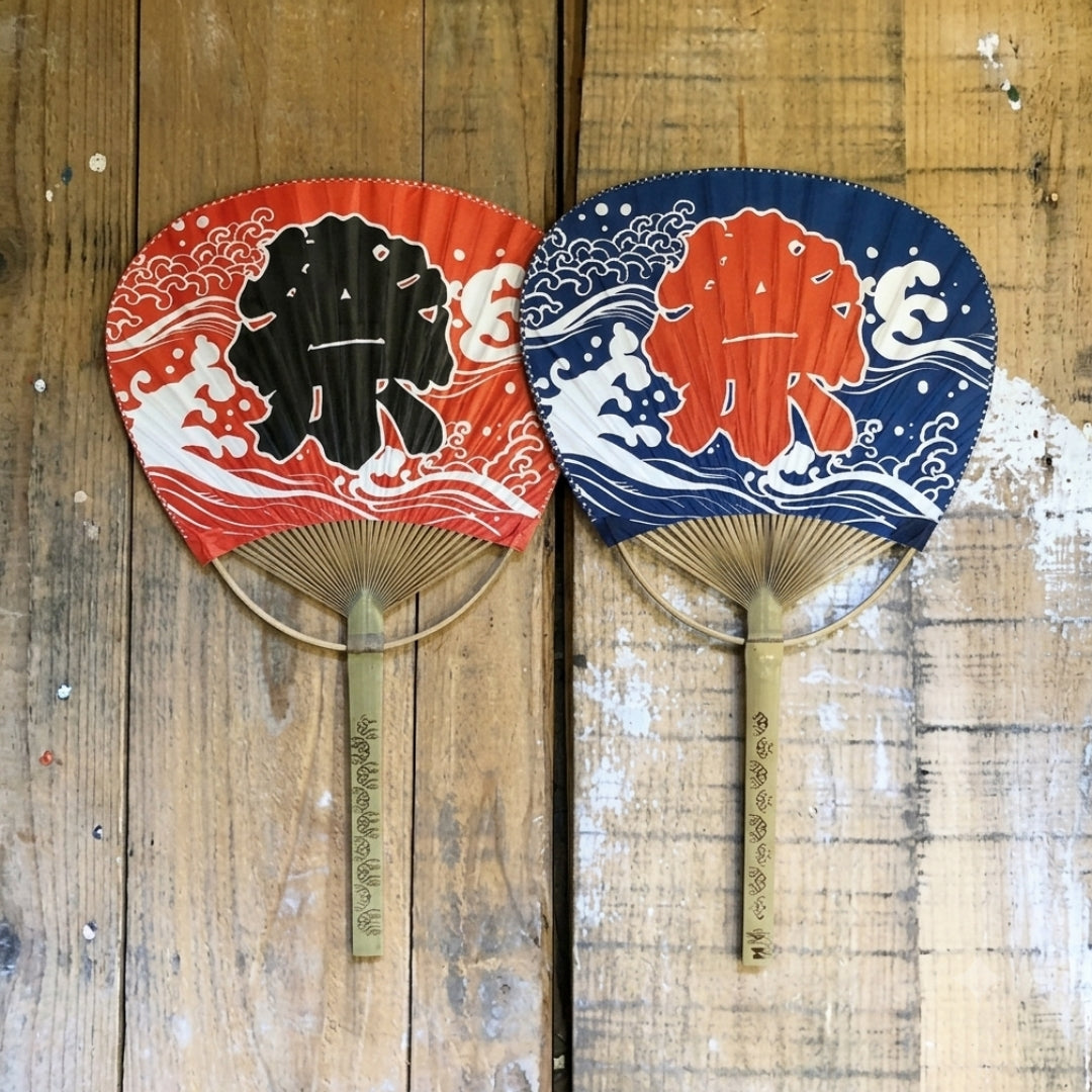 Deux éventails japonais à manche en bambou, modèles rouge et bleu avec motif de vagues stylisées.