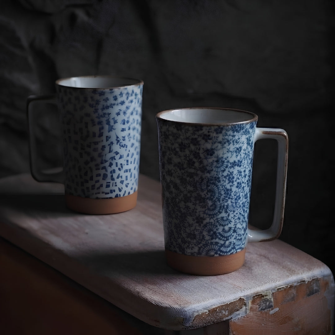 Deux mugs en céramique japonaise à motifs floraux bleus dans une ambiance chaleureuse.