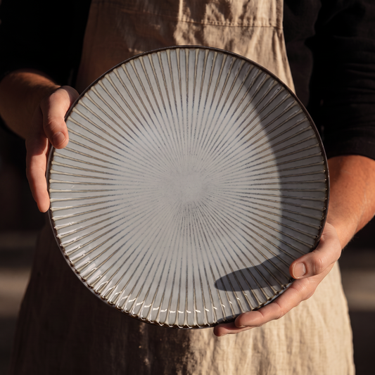 Assiette Yugen lab en céramique blanche de 24 cm avec fines rayures gris-brun rayonnantes et bordure sombre contrastée