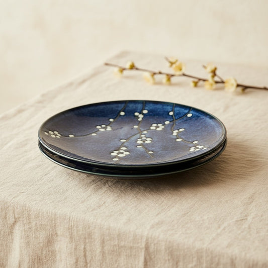 Set de 2 assiettes Yugen lab en céramique bleue avec motif de fleurs de cerisier blanc sur une nappe en lin beige