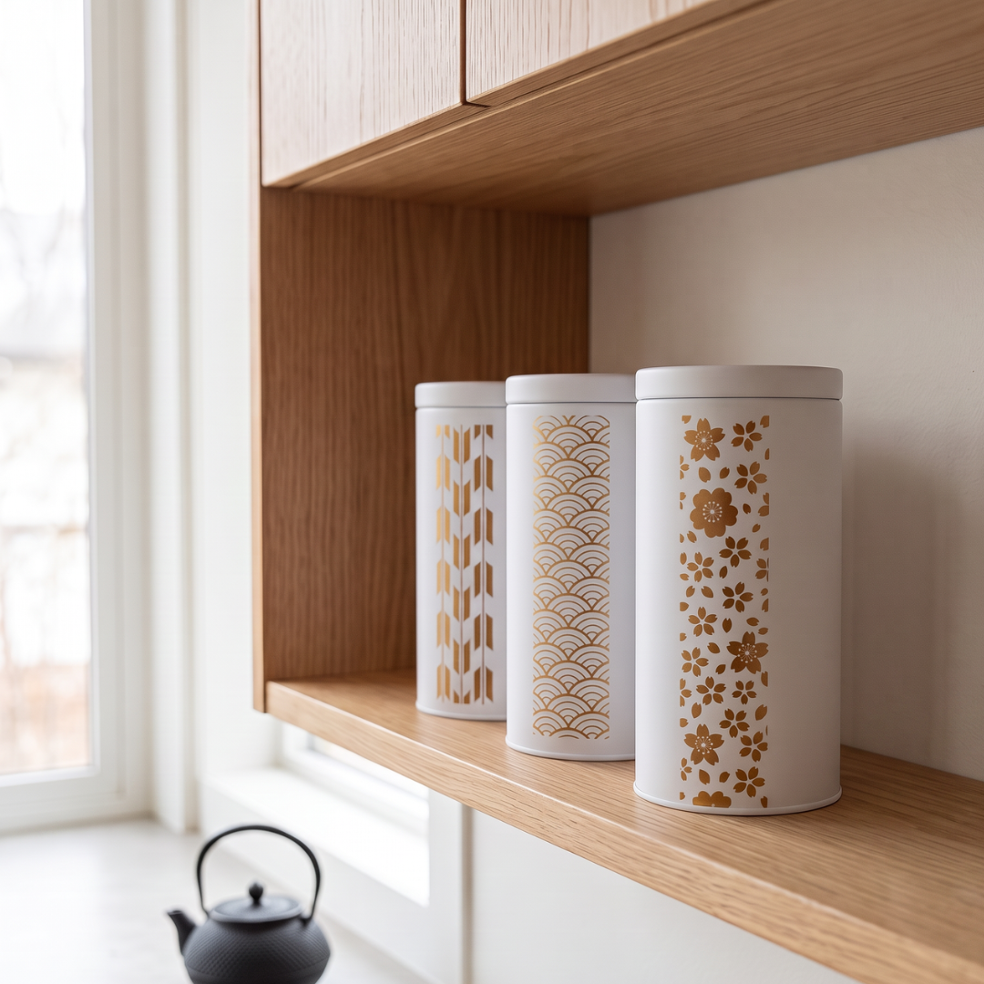Trois boîtes à thé Yugen lab en fer blanc, motifs japonais dorés Sakura, Vague et Flèche sur fond blanc, sur étagère.