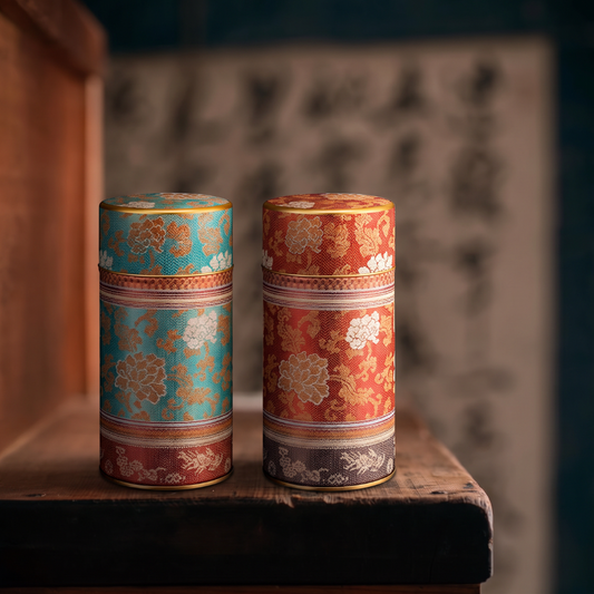 Deux boîtes à thé Yugen lab cylindriques en fer blanc avec motifs floraux japonais, coloris bleu-vert et rouge brique.