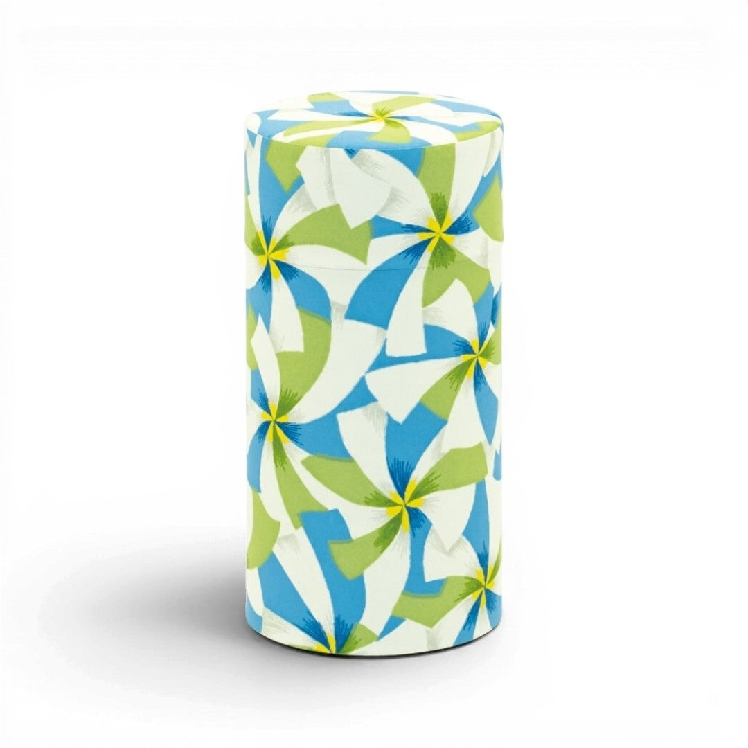 Boîte à thé Yugen lab cylindrique en fer blanc et papier washi avec motif graphique bleu, vert, blanc et jaune.