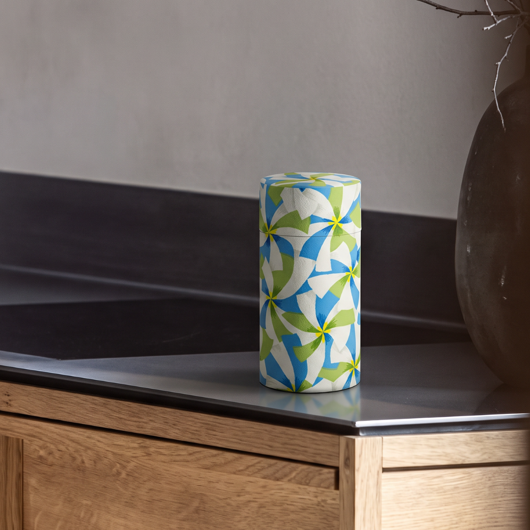 Boîte à thé Yugen lab cylindrique en fer et papier washi avec motifs graphiques bleus, verts et jaunes.