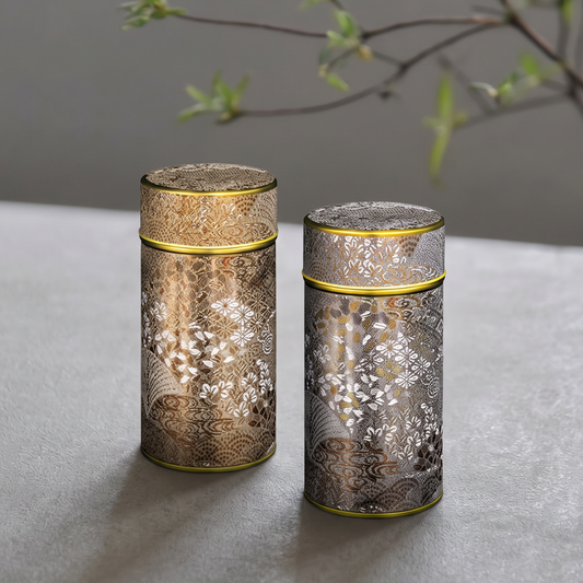 Deux boîtes à thé Yugen lab en fer blanc, forme cylindrique avec motifs floraux japonais dorés, argentés et cuivrés.