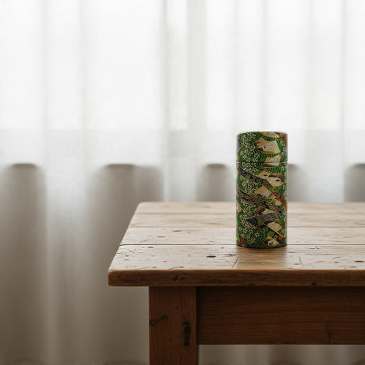 Boîte à thé Yugen lab cylindrique en fer et papier washi vert avec motifs d'éventails japonais dorés sur une table