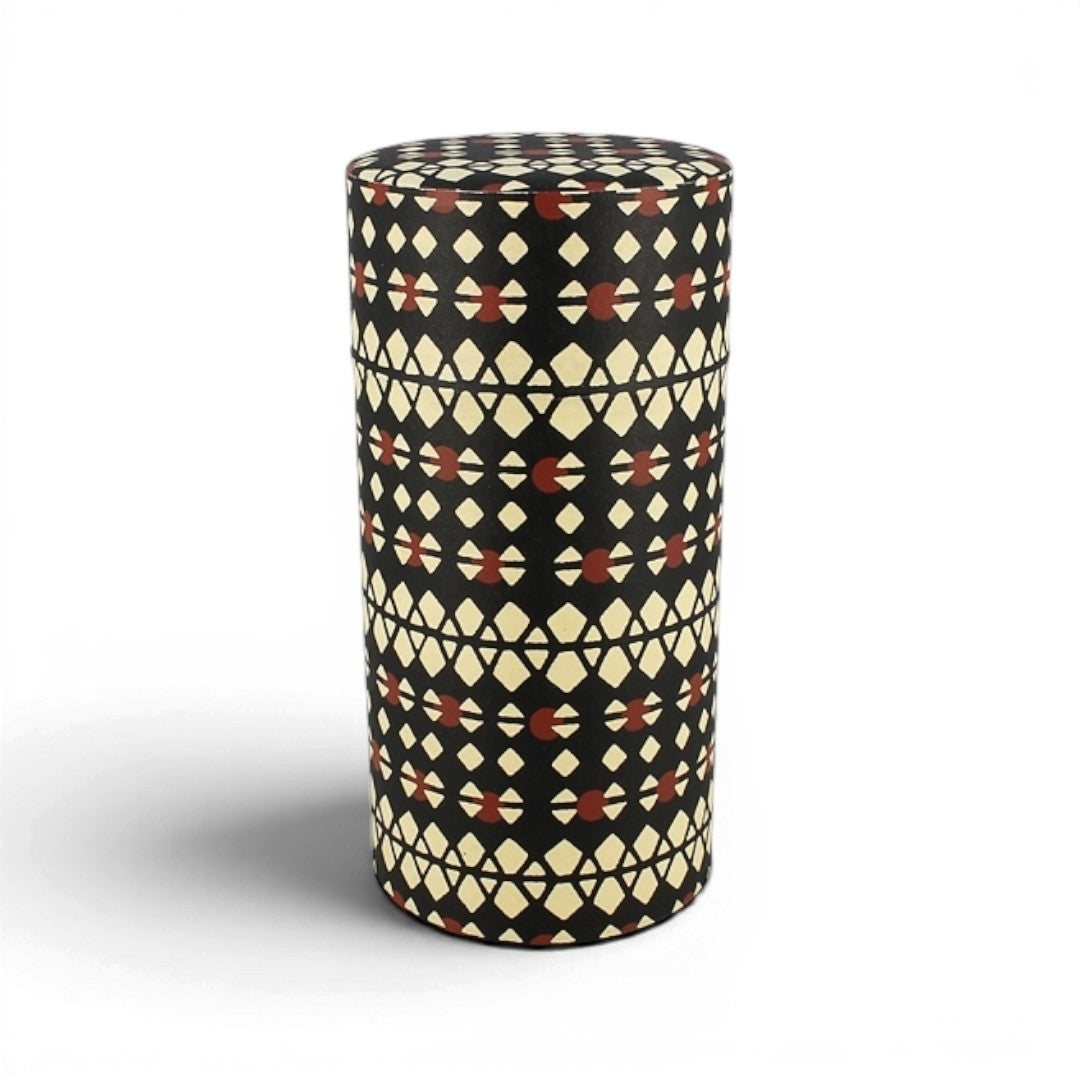 Boîte à thé Yugen lab cylindrique en fer blanc et papier washi noir, écru et rouge à motifs géométriques.