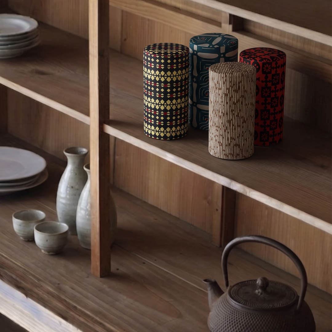 Quatre boîtes à thé cylindriques Yugen lab en fer blanc et papier washi à motifs graphiques sur une étagère en bois.