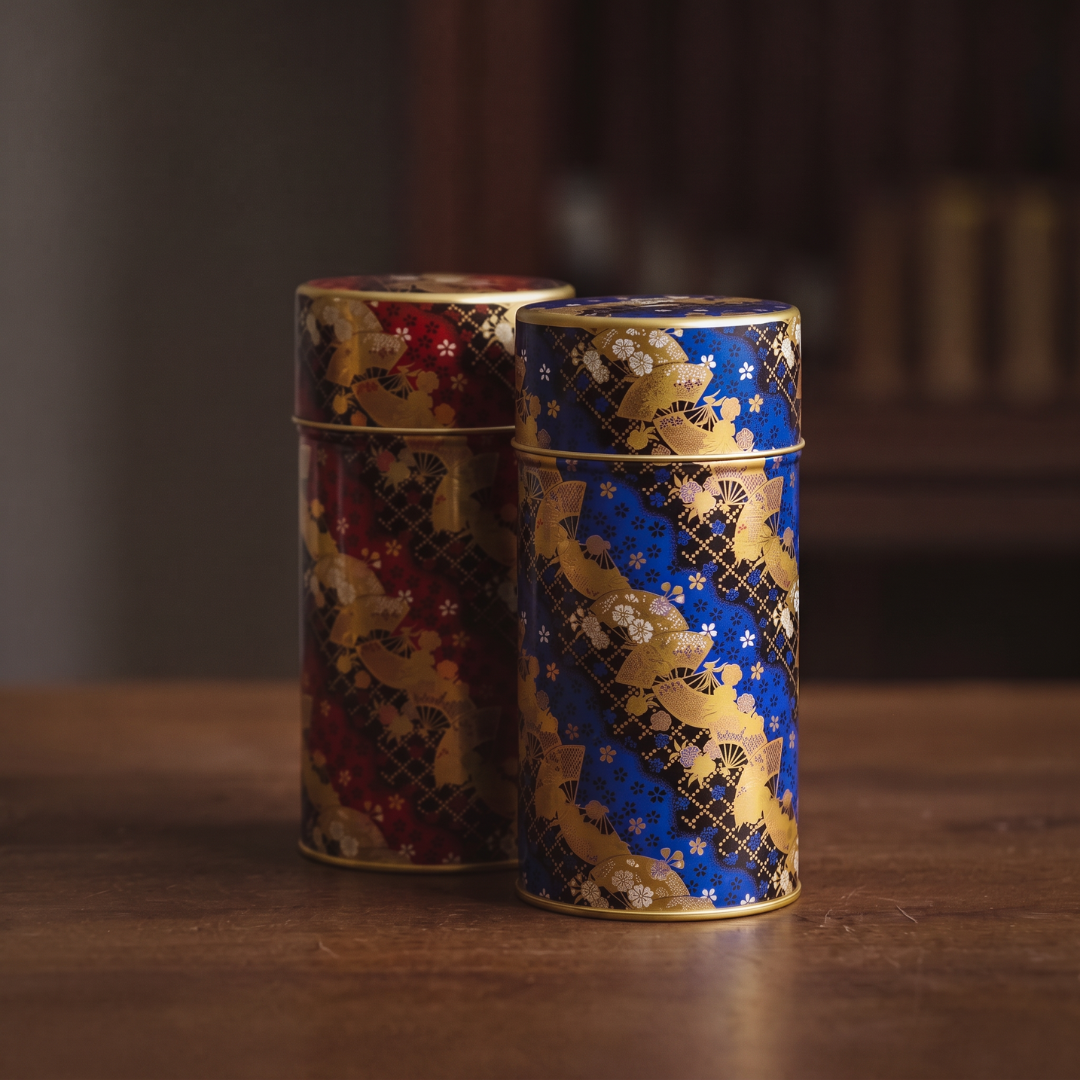 Boîtes à thé Yugen lab cylindriques en fer blanc avec motifs d'éventails dorés, coloris bleu et bordeaux sur table