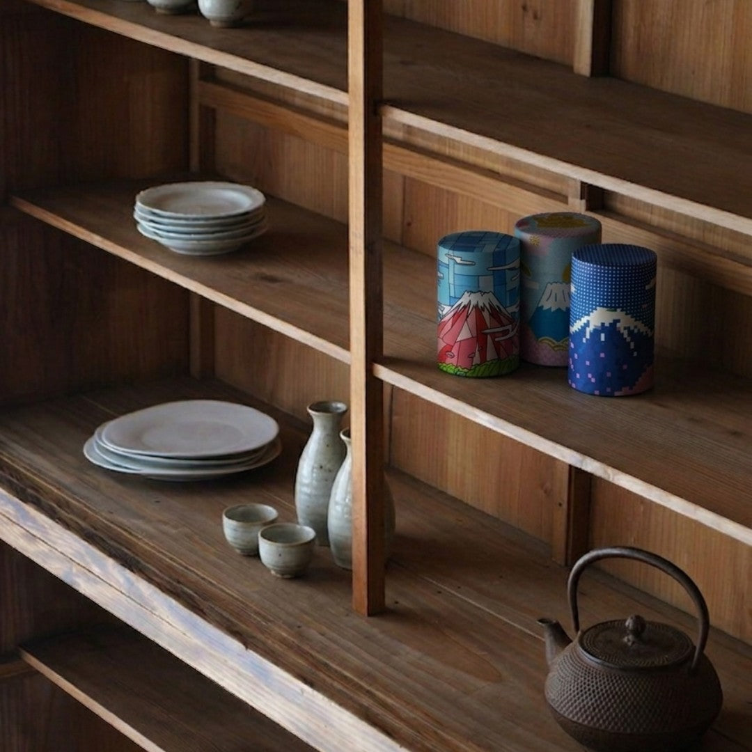 Trois boîtes à thé Yugen lab en papier washi décorées du Mont Fuji sur une étagère en bois avec de la vaisselle japonaise.