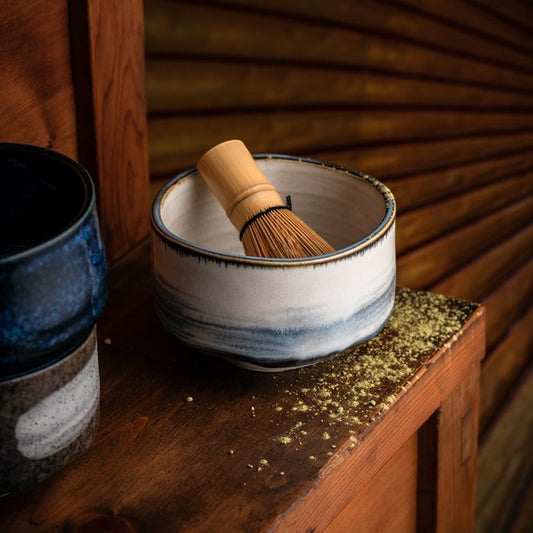 Bol à matcha Yugen lab en céramique artisanale blanc et bleu avec un fouet en bambou sur une table en bois