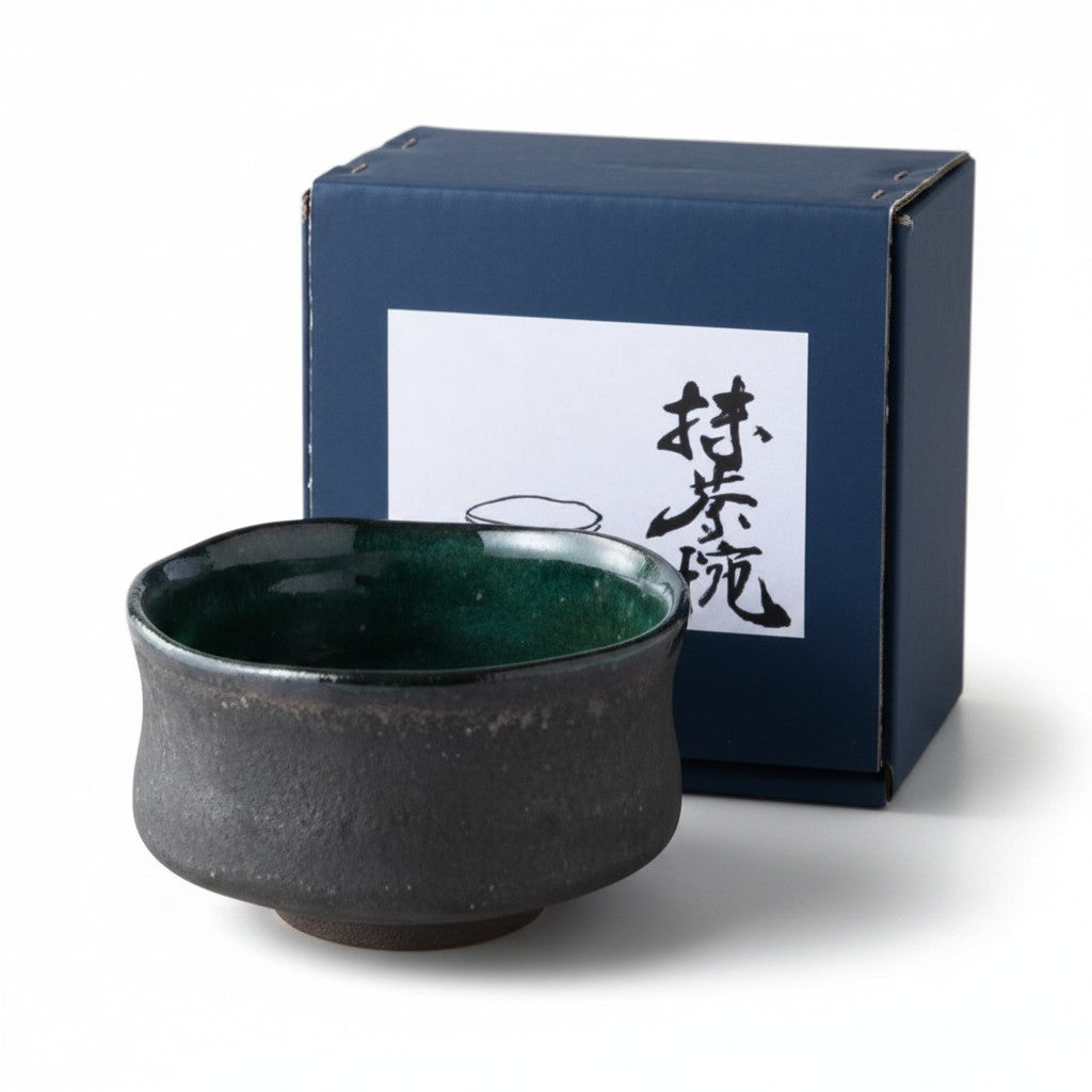 Bol matcha Yugen lab en céramique noire texturée avec intérieur émaillé vert émeraude, style wabi-sabi, devant sa boîte.