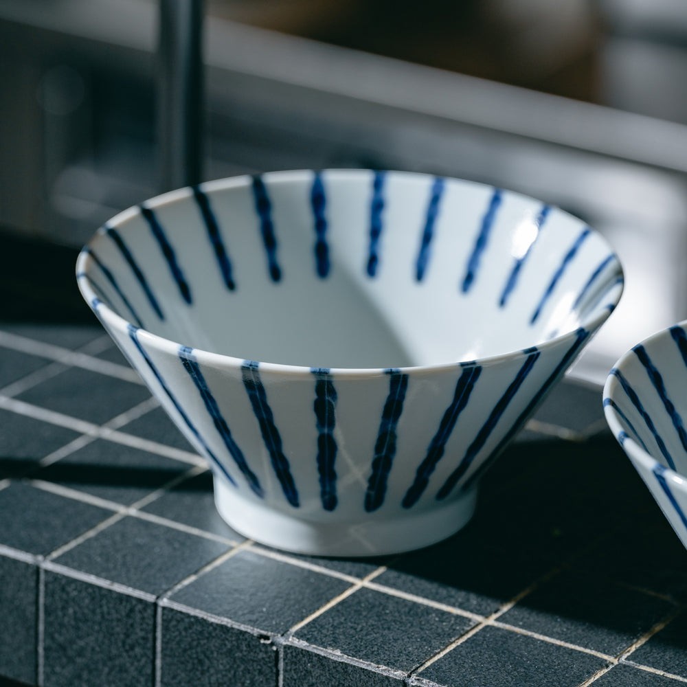Bol à ramen japonais blanc à lignes verticales bleues posé sur un carrelage sombre