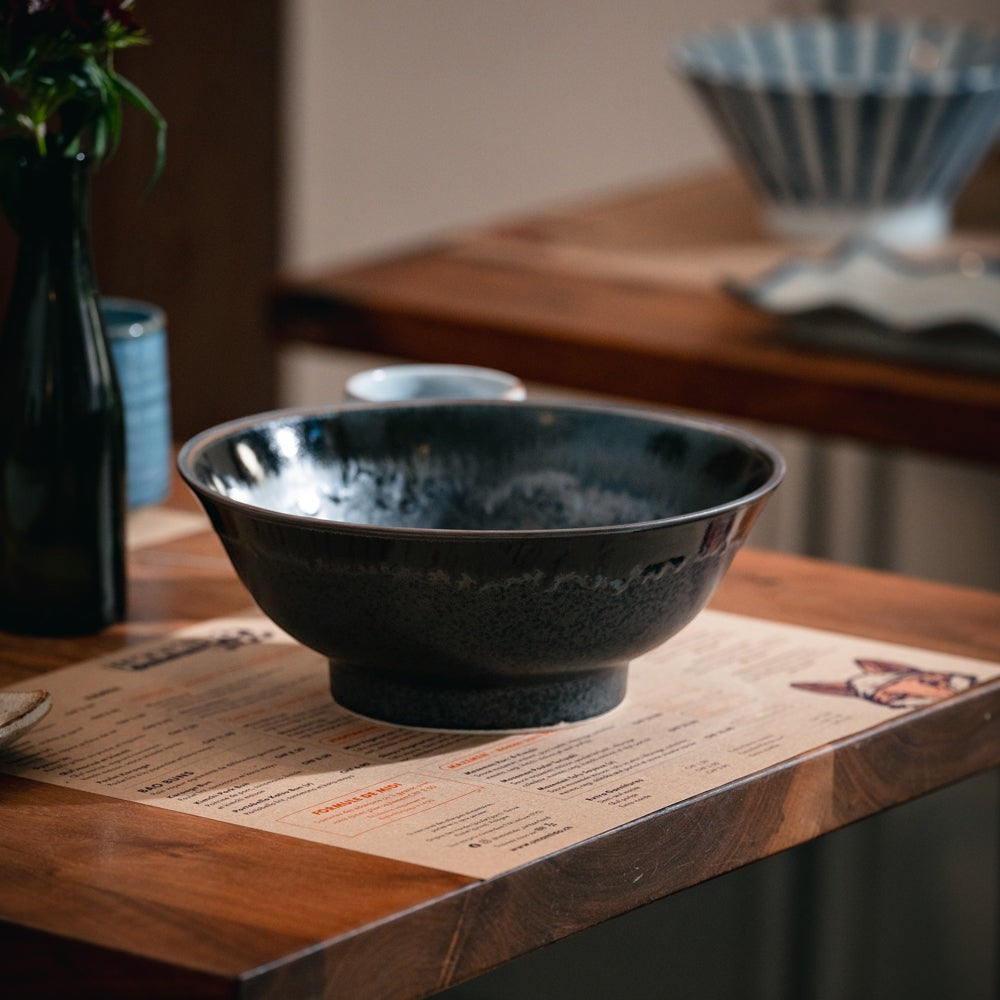 Bol à ramen noir Yugen lab au design authentique posé sur une table en bois dans une ambiance de restaurant japonais