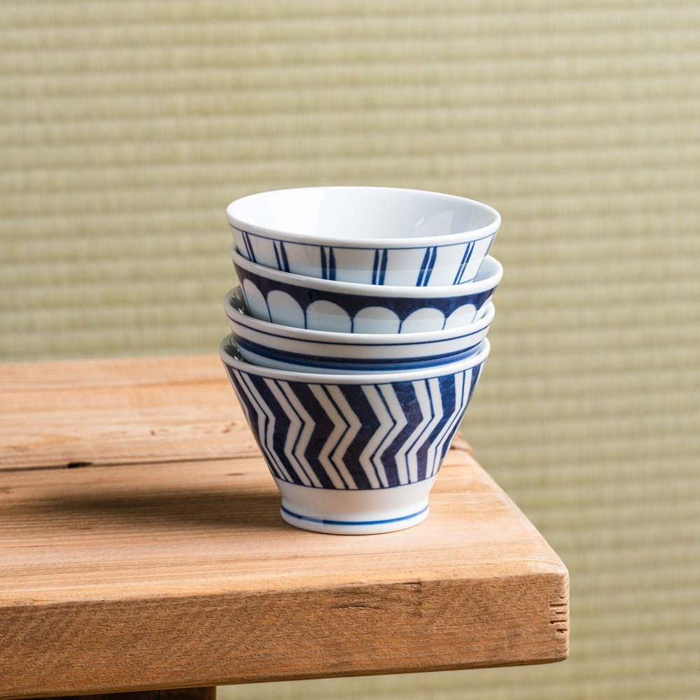 Set de 4 bols Yugen lab en porcelaine japonaise blanche avec motifs géométriques bleus empilés sur une table en bois