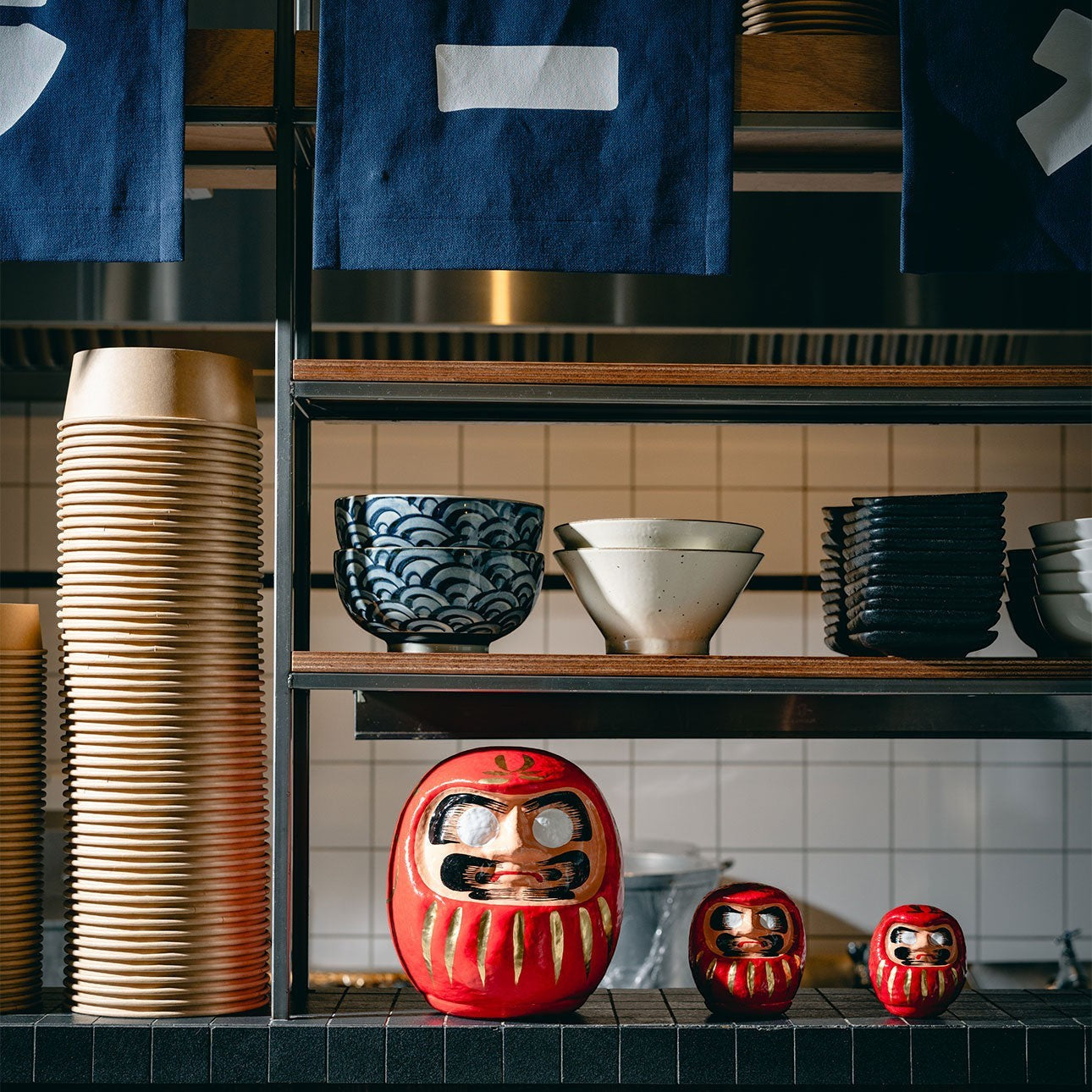 Trois figurines Daruma rouges Yugen lab en papier mâché de tailles différentes sur une étagère de cuisine japonaise