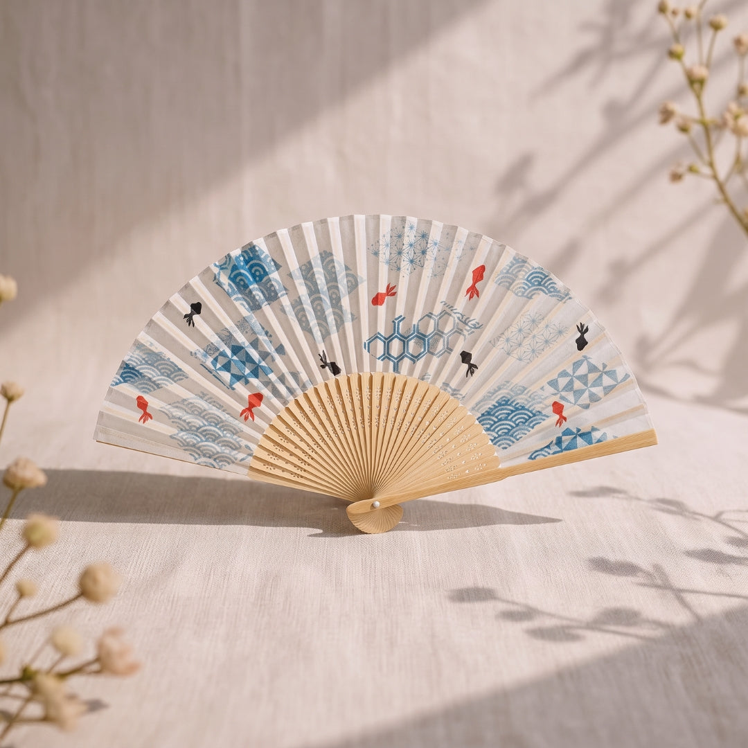 Éventail japonais Yugen lab en bambou et polyester avec motifs de poissons rouges et vagues bleues sur fond écru.