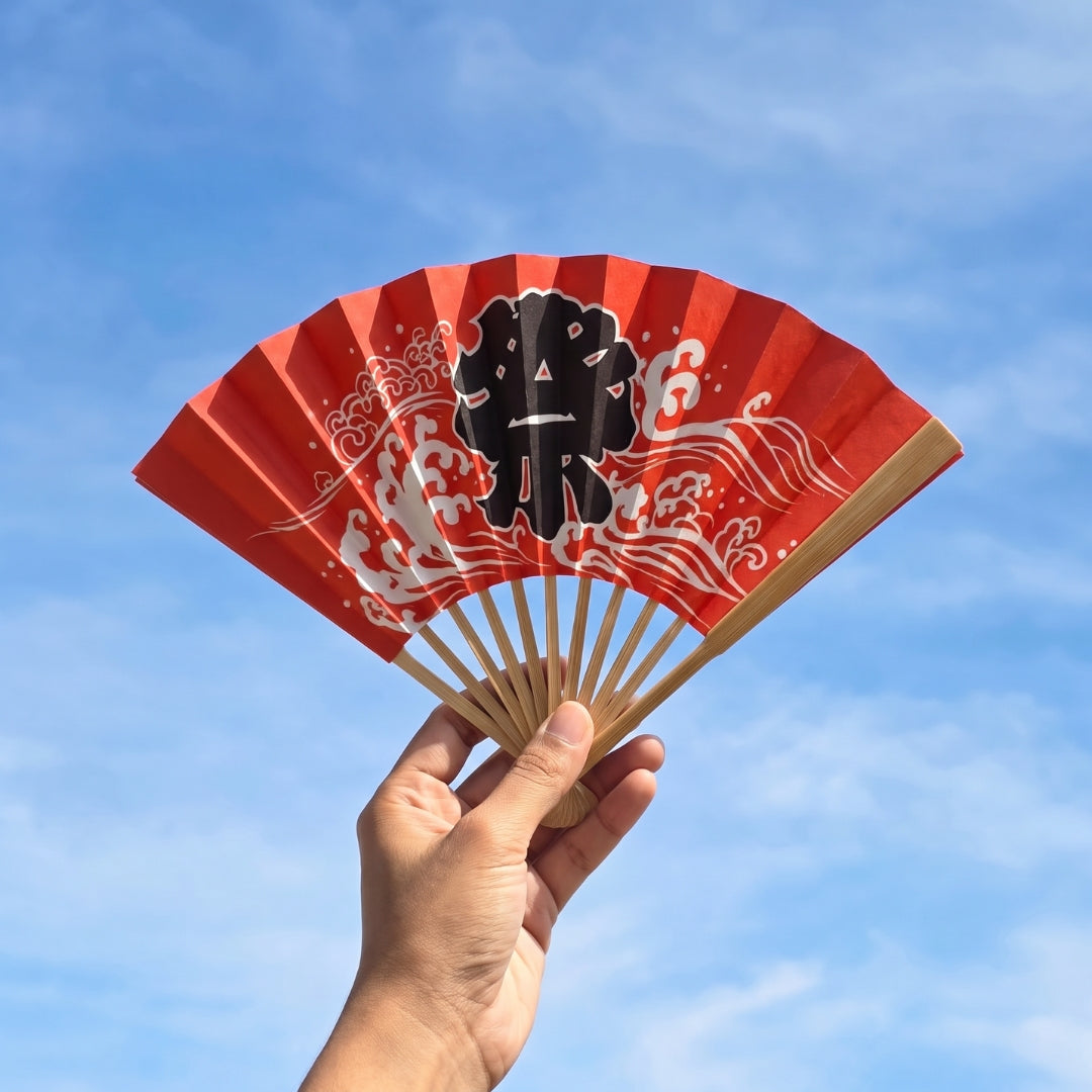 Éventail Yugen lab rouge en bambou et papier avec motif de vagues japonaises et kanji noir matsuri tenu à la main