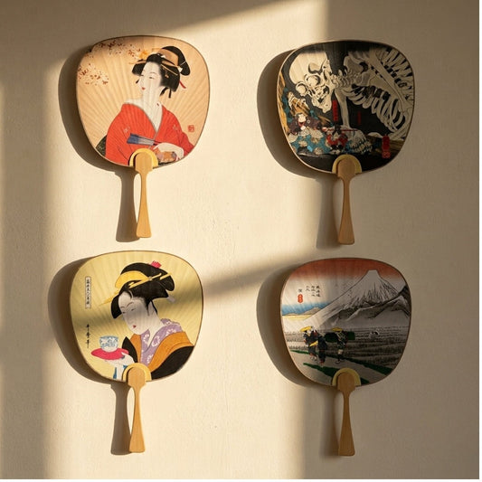 Quatre éventails Yugen lab en papier et bambou avec motifs traditionnels japonais exposés sur un mur clair.