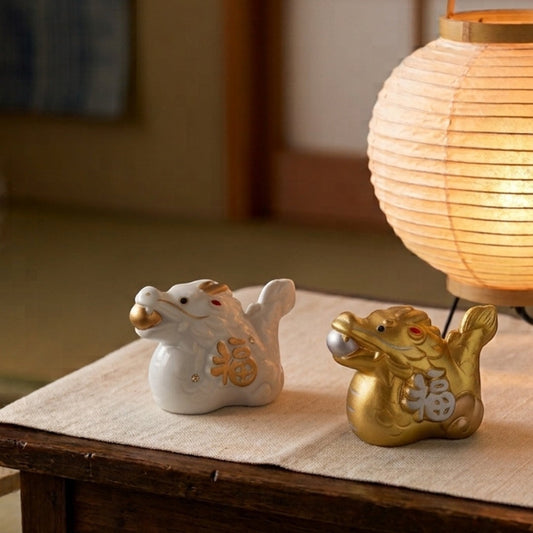 Figurines dragon Yugen lab en porcelaine blanche et dorée, style japonais, posées sur une table près d'une lanterne.