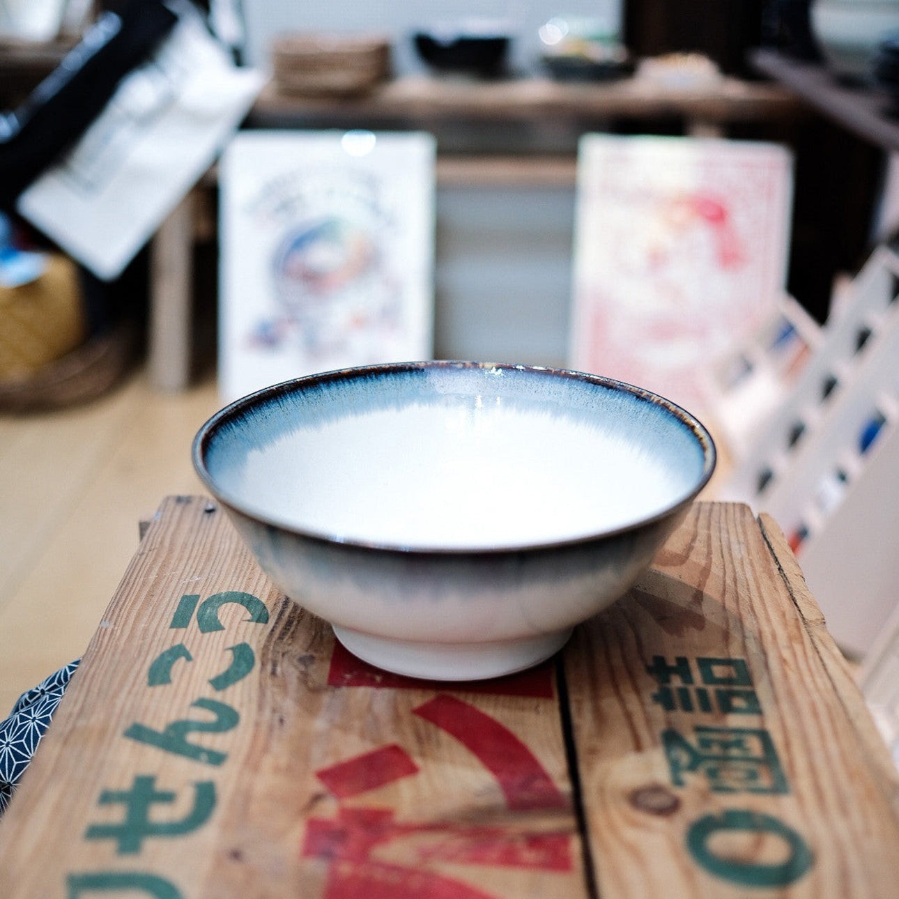 Grand bol japonais en céramique blanche Yugen lab avec un bord bleu dégradé, posé sur une caisse en bois