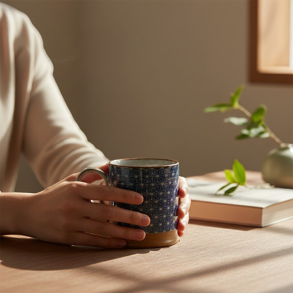 Mug Yugen lab en céramique bleue avec motif traditionnel japonais Asanoha tenu par des mains sur une table en bois