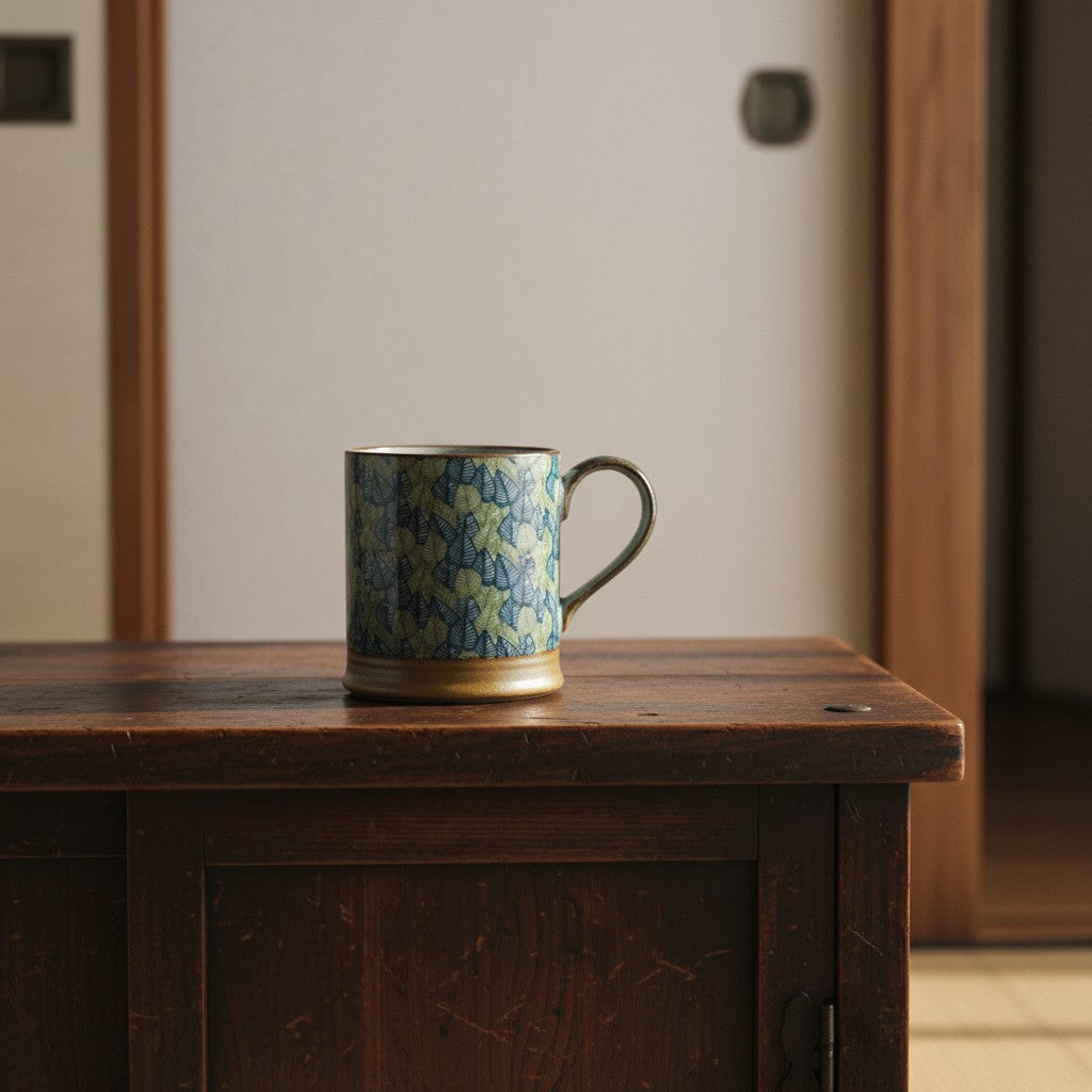 Mug Yugen lab en céramique avec motif de feuilles japonaises bleues et vertes posé sur une table en bois rustique