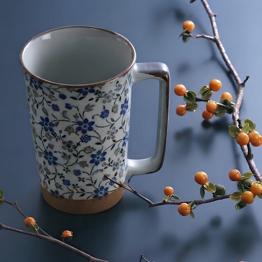 Mug en céramique Yugen lab avec motifs floraux bleus et gris, anse rectangulaire et base en terre cuite naturelle.
