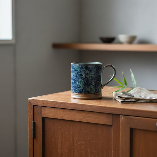 Mug Yugen lab en céramique bleu avec motif éventail traditionnel posé sur un meuble en bois