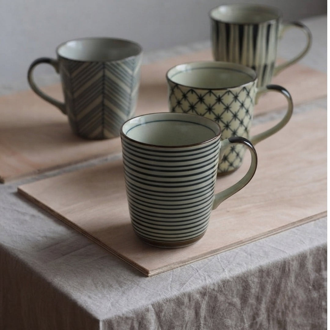 Quatre mugs Yugen lab en porcelaine ivoire avec motifs graphiques noirs d'inspiration japonaise sur une table.