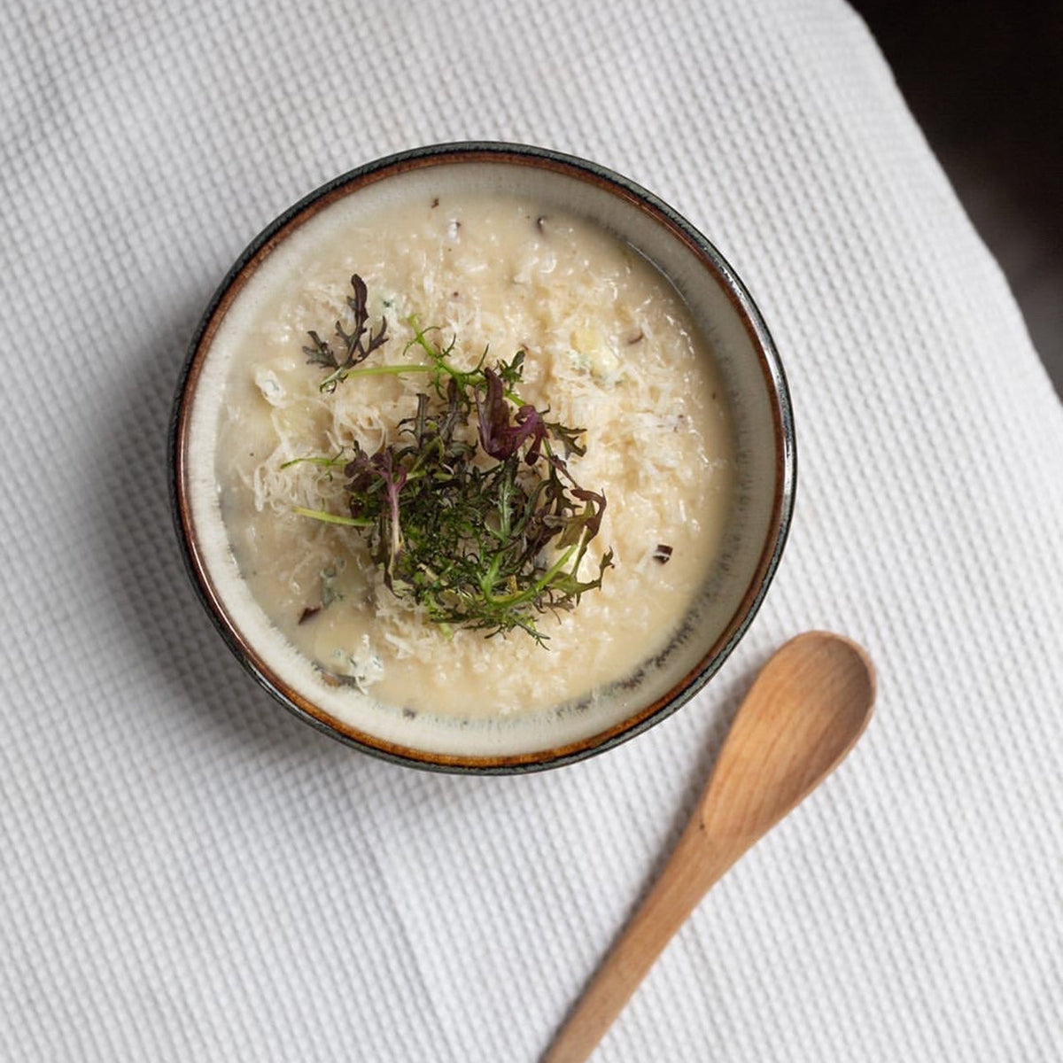 Petite assiette japonaise ronde Yugen lab bicolore noir et blanc contenant un plat crémeux avec des herbes fraîches