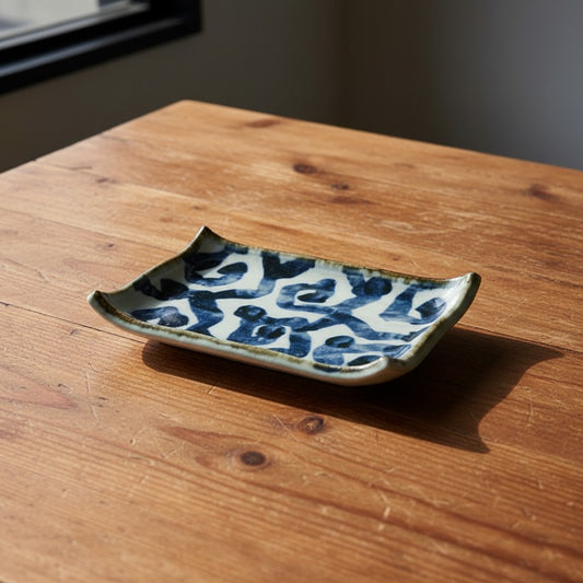 Plat à sushi Yugen lab en céramique blanche avec motifs traditionnels bleus et bords incurvés sur table en bois