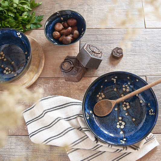 Saladier Yugen lab en céramique bleue avec motifs de branches de cerisiers blancs sur une table en bois rustique