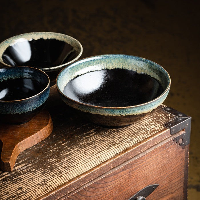 Saladier Yugen lab en porcelaine japonaise noire avec une bordure verte artisanale posé sur un coffre en bois ancien