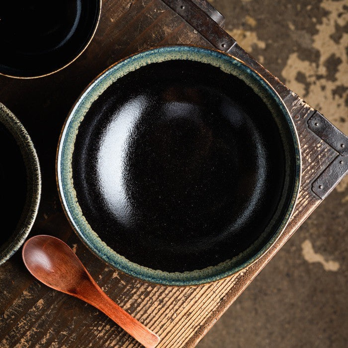 Saladier Yugen lab en porcelaine japonaise noire avec une bordure verte artisanale, posé sur une table en bois.