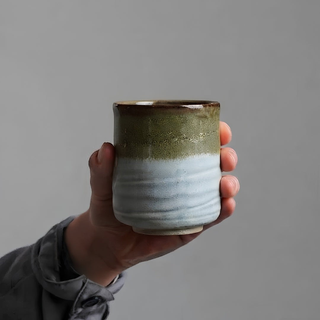 Tasse à thé Yugen lab Hagi en céramique blanche et vert olive tenue en main, style wabi-sabi artisanal.