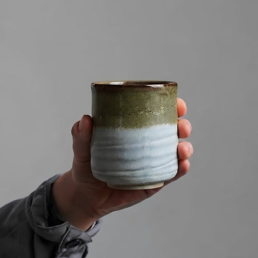 Tasse à thé Yugen lab Hagi en céramique blanche et vert olive tenue en main, style wabi-sabi artisanal.