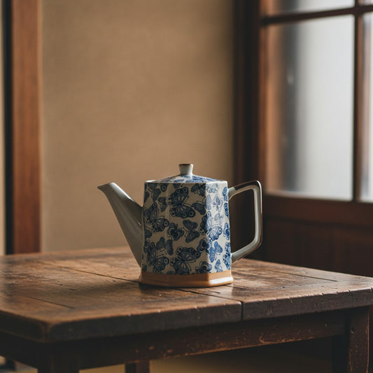 Théière japonaise Yugen lab en céramique blanche et bleue avec motif papillons sur une table en bois rustique